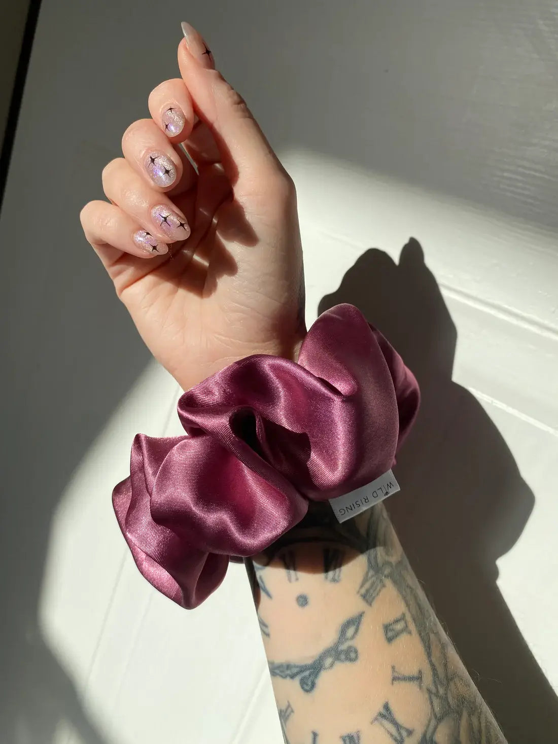 Hand wearing a pink satin scrunchie with a neutral background