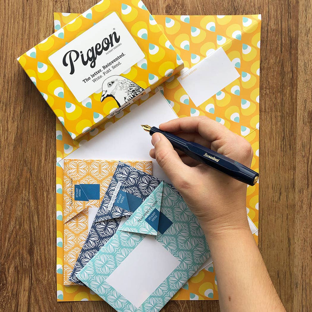 Hand holding a pen over stationery items with a 'Pigeon' product on a wooden surface